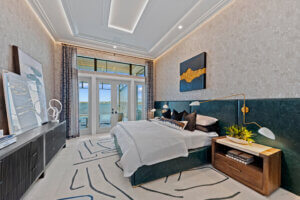 Luxury-model-home master bedroom with waterfront balcony access, designer lighting, and custom headboard wall.