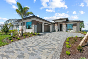 Modern luxury model home with three-car garage and stone-accented entryway under a blue sky.