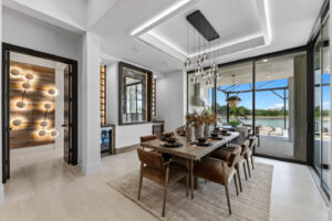 Modern dining room with a large wooden table and brown chairs, overlooking a water view through glass sliding doors.