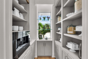 Walk-in pantry in a custom built home featuring organized shelving, built-in storage, and a central window bringing in natural light with views of greenery outside.