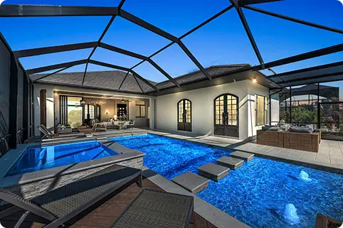 Outdoor pool area of a luxury home with screened enclosure, spa pool, lounge chairs, and covered patio seating.