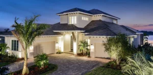 Elegant coastal home with palm landscaping, stone driveway, and warm exterior lighting