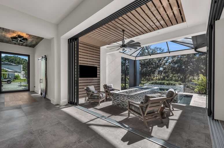 Outdoor living space with a fireplace, seating area, and large windows overlooking a landscape.
