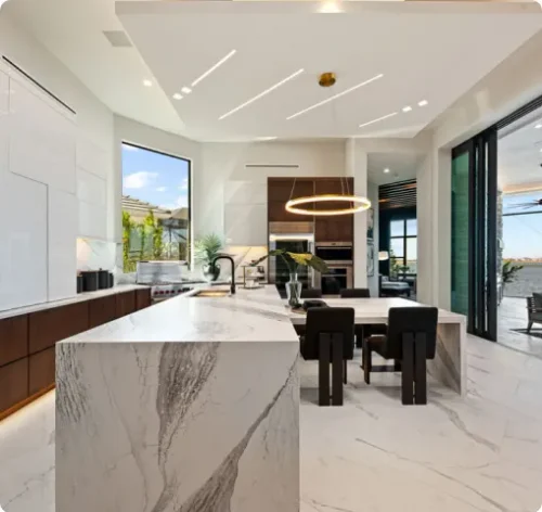Open concept kitchen inside luxury homes in Florida with a marble island, modern pendant lighting, and spacious layout.